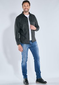 Black plaid button-up shirt, white undershirt, blue jeans, and black shoes. The shirt features two chest pockets and a classic collar.