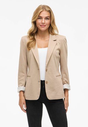 Beige blazer med slåede klapper, to forlommer og to knapper. Har oprevne stribede ærmer og er lavet af letvægtsstof.