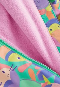 Kolorowa kurtka zapinana na zamek z różowym polarem od wewnątrz i wzorzystą zewnętrzną częścią z abstrakcyjnymi kształtami w kolorach zielonym, żółtym i pomarańczowym.