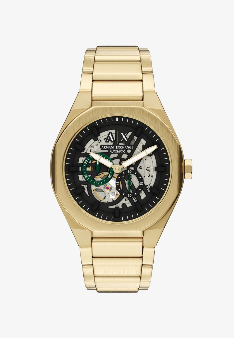 Montre-bracelet en métal doré avec cadran squelette noir, aiguilles blanches, sous-cadrans verts et marquage Armani Exchange, mouvement automatique visible.