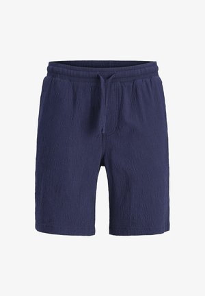 Granatowa koszula z krótkim rękawem i dopasowanymi szortami z fakturowanej tkaniny. Zawiera białe guziki i luźny krój. Noszona z białymi sneakersami.