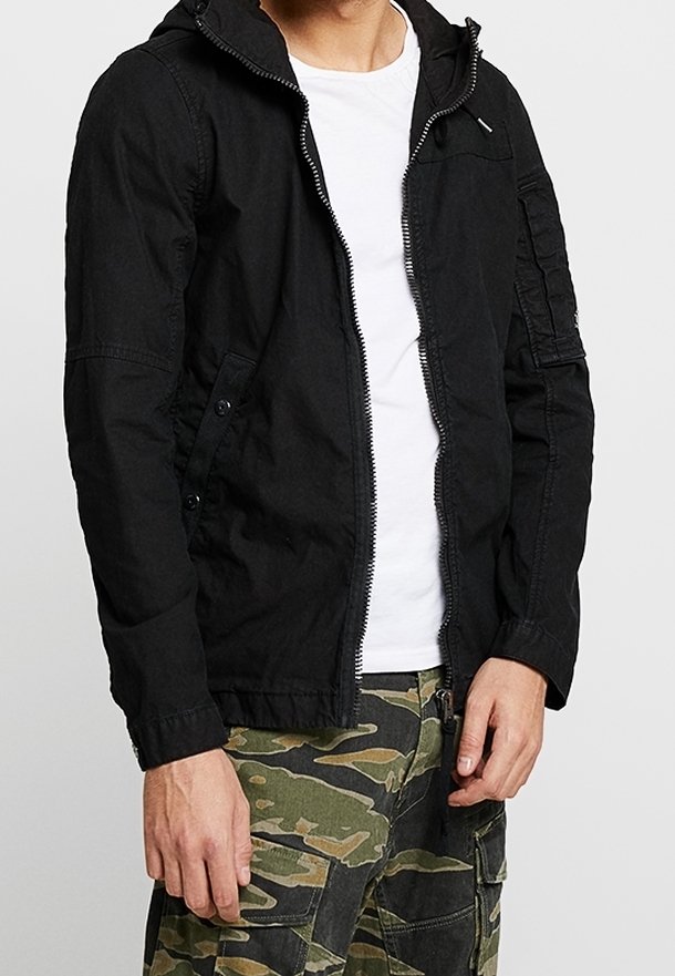 Veste à capuche légère noire avec fermeture éclair, boutons-pression sur les poches et coupe décontractée, assortie à un pantalon cargo en camouflage.