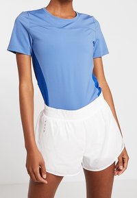 Blå idrottstopp med korta ärmar och rund halsringning, kombinerad med vita lätta löparshorts med elastisk midja.