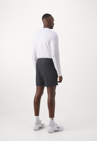 Conjunto atlético que incluye una camiseta blanca de manga larga y pantalones cortos negros. Los pantalones cortos tienen una cintura elástica y bolsillos laterales. Zapatillas blancas con detalles.