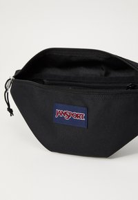 Borsa nera in tessuto con chiusura a zip e logo Jansport. Presenta una superficie strutturata e un design elegante e angolare. L'interno è semplice.