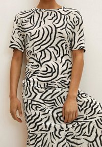 Femme portant un haut à manches courtes et une jupe à volants avec un motif abstrait noir et blanc de zèbre, se tenant devant un fond uni.