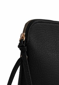 Černá texturovaná kožená kabelka se zlatým zipem a kováním. Má tenký, nastavitelý popruh a hladký, elegantní tvar.