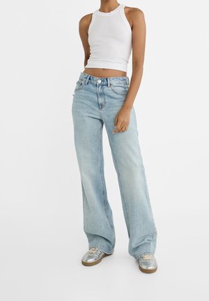 Light blue, wide-leg jeans with a faded finish, five pockets, and a front button closure, paired with a white cropped tank top.