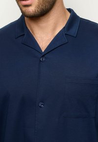 Camisa de manga corta en color navy, diseño abotonado, cuello con muesca, tela suave, bolsillo en el pecho y botones a juego.