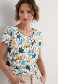 Korte mouw bloemen top met een ronde halslijn, met een kleurrijk patroon van blauwe, gele en grijze bloemen op een witte achtergrond.