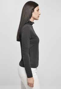 Svart langermet turtleneck-genser, glatt stoff, tettsittende design med en strømlinjeformet silhuett og rene linjer, kombinert med hvite bukser.