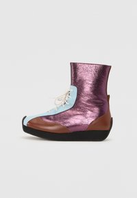 Bota metálica púrpura con punta de cuero azul, acentos marrones y cordones blancos. Presenta un diseño de caña alta y una superficie texturizada.