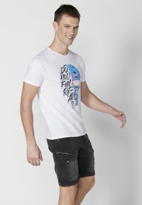 White short-sleeve t-shirt with colorful graphic text "DO YOU FEEL REAL?" and a face design. Paired with black cargo shorts featuring zipped pockets.