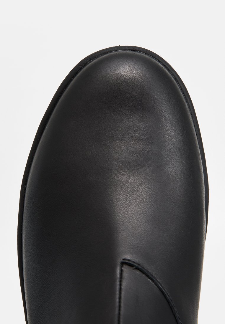 Schwarze glatte Lederstiefel mit abgerundetem Zehenbereich und sichtbaren Nahtdetails vor einem schlichten hellen Hintergrund.