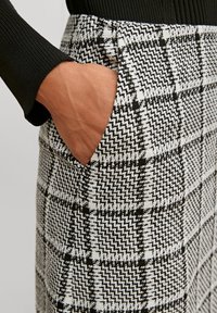Black and white plaid skirt with a textured woven fabric, featuring side pockets and a mid-rise waist. Close-up on hand in pocket.