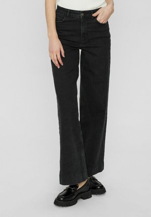 Wide-leg black denim jeans featuring a high waist, classic five-pocket design, and a slightly faded finish. Worn with black chunky shoes.