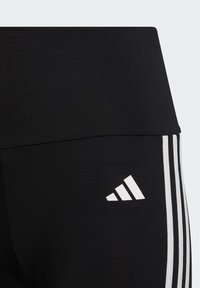 Leggings deportivos negros con una textura suave, que presentan tres rayas blancas a lo largo del costado y un logo blanco en la cinturilla.