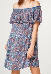 Robe dénudée sur les épaules avec un décolleté à volants, présentant un motif paisley vibrant en bleu, rose et blanc sur un tissu léger.