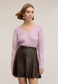 Maglione lavorato a maglia di colore viola chiaro con scollo a V e motivo a trecce, abbinato a una gonna svasata in finta pelle marrone. Tessuto liscio, vestibilità casual.