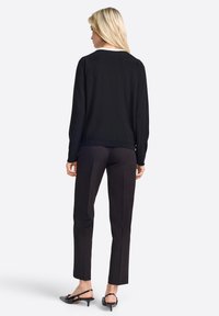 Zwarte trui met een ronde halslijn, gecombineerd met zwarte tapered broeken en lage zwarte slingback schoenen, gezien vanaf de achterkant.
