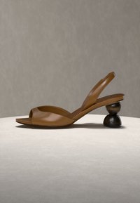 Καφέ δερμάτινο σανδάλι τύπου slingback με ανοιχτά δάχτυλα και μοναδικό στρογγυλό δίπτυχο ξύλινο τακούνι σε ουδέτερο φόντο.