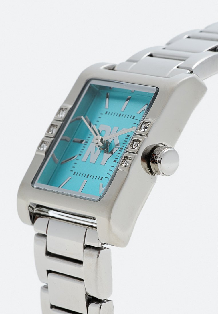 Silberne Metall-Armbanduhr mit rechteckigem türkisfarbenem Ziffernblatt, Kristallakzenten sowie silbernen Stundenmarkierungen und -zeigern, die 10:12 anzeigen.