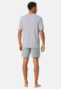 Gray cotton t-shirt paired with patterned shorts featuring blue geometric shapes. Model is barefoot, viewed from the back.