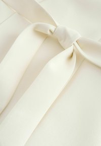 Cream fabric detail with a tied bow accent at the center. Smooth texture with soft drapes and a minimalist design.