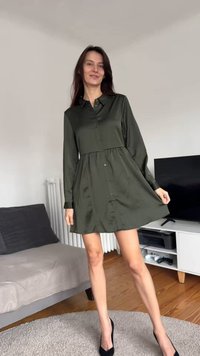 Abito verde scuro con bottoni, maniche lunghe, vita raccolta, texture liscia e gonna svasata. Indossato con tacchi neri.