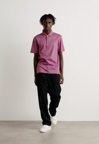 Rozā polo krekls ar īsām piedurknēm un apkakli, apvienots ar melnajām biksēm un baltajām kedām. Gluda auduma un pieguļošs dizains.