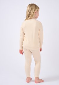 Completo termico beige composto da un top a maniche lunghe e leggings aderenti. Tessuto a coste, morbido e con polsini elasticizzati ai polsi e alle caviglie.