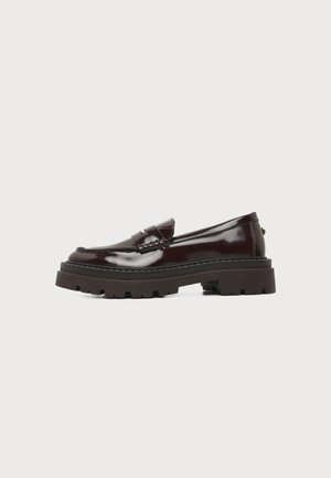 Mocasín de cuero marrón oscuro brillante con suela gruesa de taco y tacón bajo, vista lateral sobre fondo blanco.