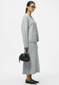 Sivi pleteni kardigan s V-izrezom i gumbima, uparen s odgovarajućom sivom suknjom. Crna torba i ravne cipele upotpunjuju odjevnu kombinaciju.