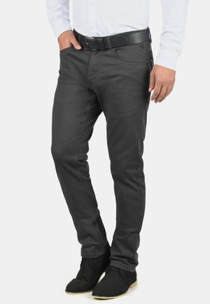 Donkergrijze spijkerbroek van denim, slim fit ontwerp, voorzien van zijzakken en een knoopsluiting, gecombineerd met zwarte enkellaarzen en een wit shirt.