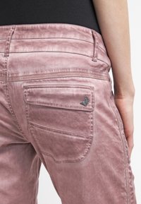 Rosa denimjeans med en mjuk textur, som har en bakficka med en accentuerad fjärilslogotyp och en subtiltvättad design.