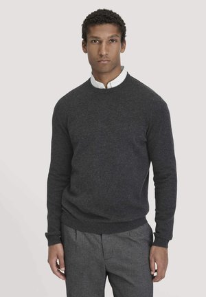 Donkergrijze ronde hals sweater van zacht breiwerk, met ribgebreide manchetten en onderkant, gedragen over een witte blouse met kraag en grijze broek.