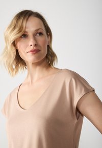 Lys beige V-hals top med korte ærmer lavet af blødt, glat stof, med minimale sømme og en afslappet pasform.