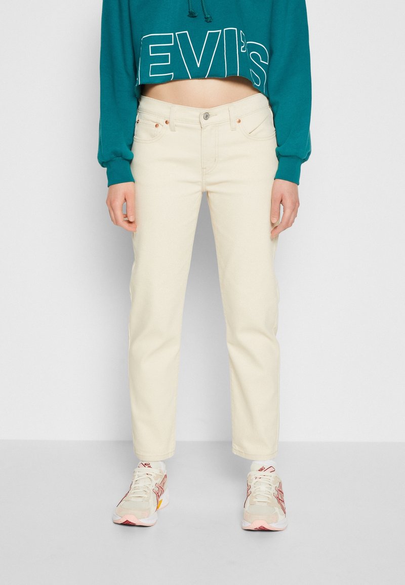 Person wearing cream-colored straight-leg jeans, teal cropped sweatshirt with "LEVI'S" text, and beige sneakers with pink and red accents.