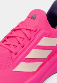 Sapatilha de atletismo rosa brilhante com riscas bege claras, parte superior em malha texturizada, atacadores rosas e um logo preto na lingueta.