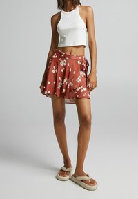Gonna avvolgente marrone a fiori con orlo asimmetrico, abbinata a un crop top bianco a coste e sandali slip-on beige.