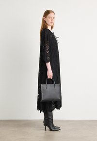 Black lace dress with a loose fit and 3/4 sleeves. Worn with tall black heeled boots and holding a structured black leather handbag.