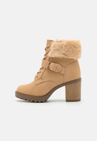 Bottine en suede tan avec un col en fausse fourrure, un devant lacé, un détail de boucle sur le côté et un talon en bois épais. Motif texturé sur le talon.