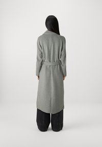Long, gray wool coat with a belted waist and lapel collar. Features a straight cut and soft texture, paired with dark wide-leg trousers.