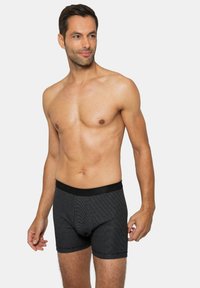 Czarne bokserki w paski z miękkim paskiem w talii, o dopasowanym kroju i gładkiej fakturze. Noszone przez modela bez koszulki.