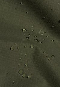 Waterdruppels die parelen op donker groen, gestructureerd waterdicht materiaal met een zichtbaar rasterpatroon.