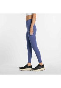 Hoge paarse leggings met een gladde textuur, voorzien van een subtiele logodetail, gecombineerd met zwarte sportschoenen.