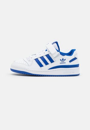 Hvid Adidas sneaker med blå striber, blå sål og en velcro-rem over hvide snørebånd, vist fra den indvendige side på hvid baggrund.