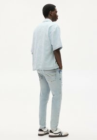 Světle modrá košile s krátkým rukávem z texturované látky, zkombinovaná se světle modrými džíny s oprýskanými detaily a kapsami. Černobílé tenisky.