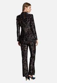 Leopardenmuster-Anzug in dunklen Tönen, bestehend aus einem taillierten Blazer und einer gut sitzenden Hose. Glänzende Textur mit sanftem Glanz, kombiniert mit hohen Schuhen.