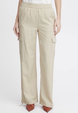 Pantalons cargo beiges avec une taille élastique, coupe ample, poches latérales et un tissu texturé. Portés avec des talons rayés orange et noir.